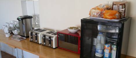 A kitchenette with a toaster, kettle, microwave, refrigerator, and various food items.