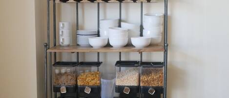 A shelf with stacked plates, bowls, and containers of snacks.