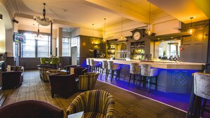 A bar area with multiple seating options, a bar counter, and a clock on the wall. - Herriots (Skipton)