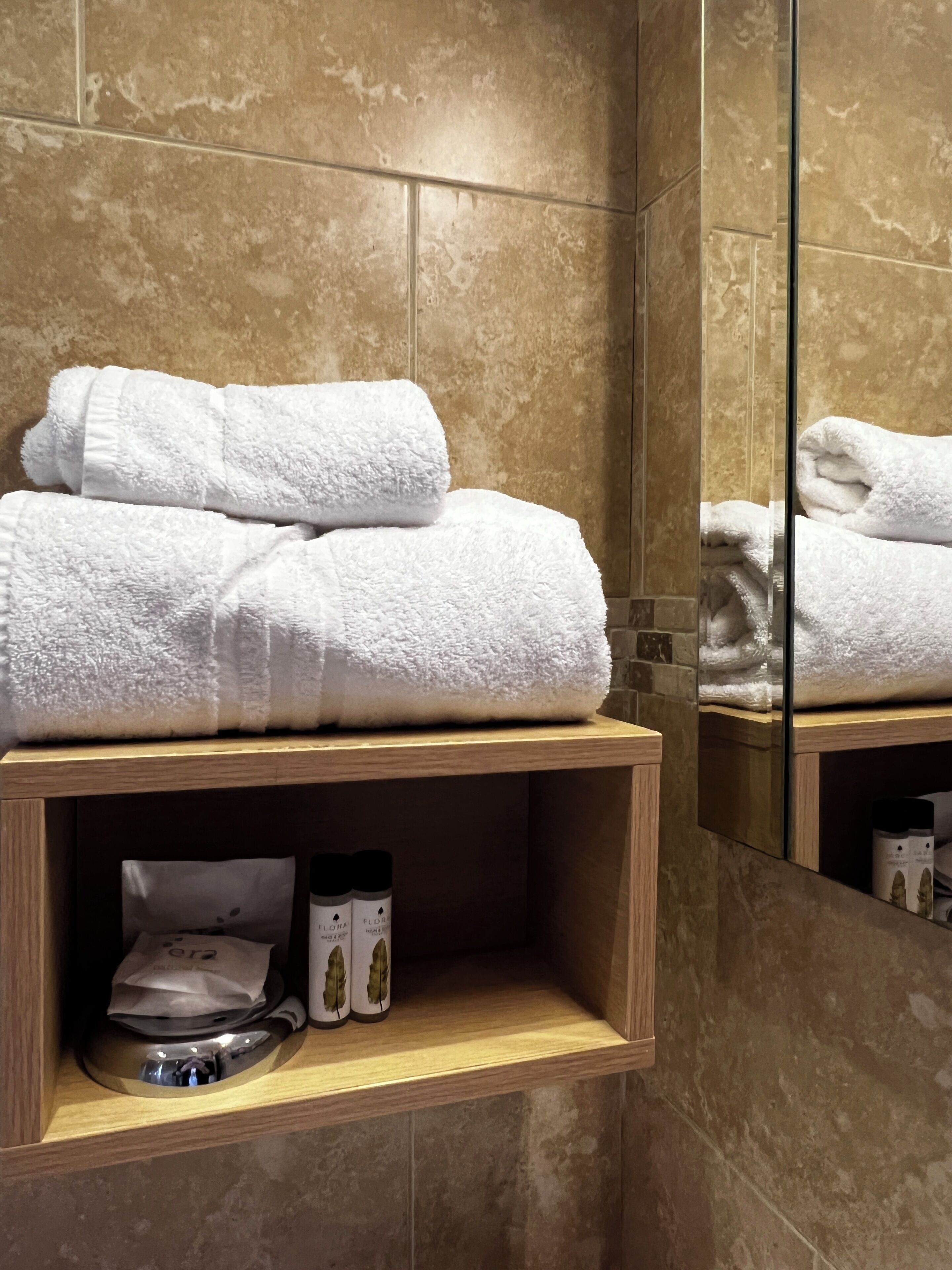 A bathroom with a wooden shelf holding folded towels and a small container.