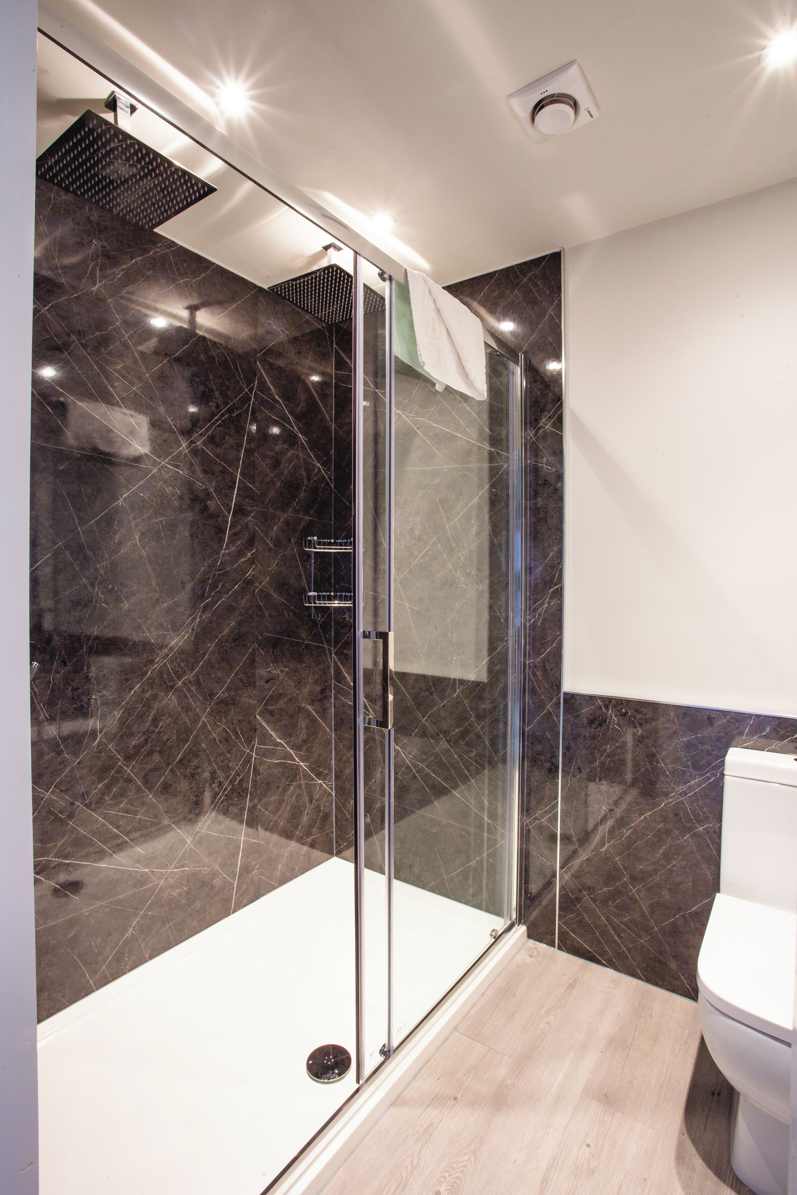 A modern bathroom with a glass-enclosed shower, a white toilet, and dark marble tiles.