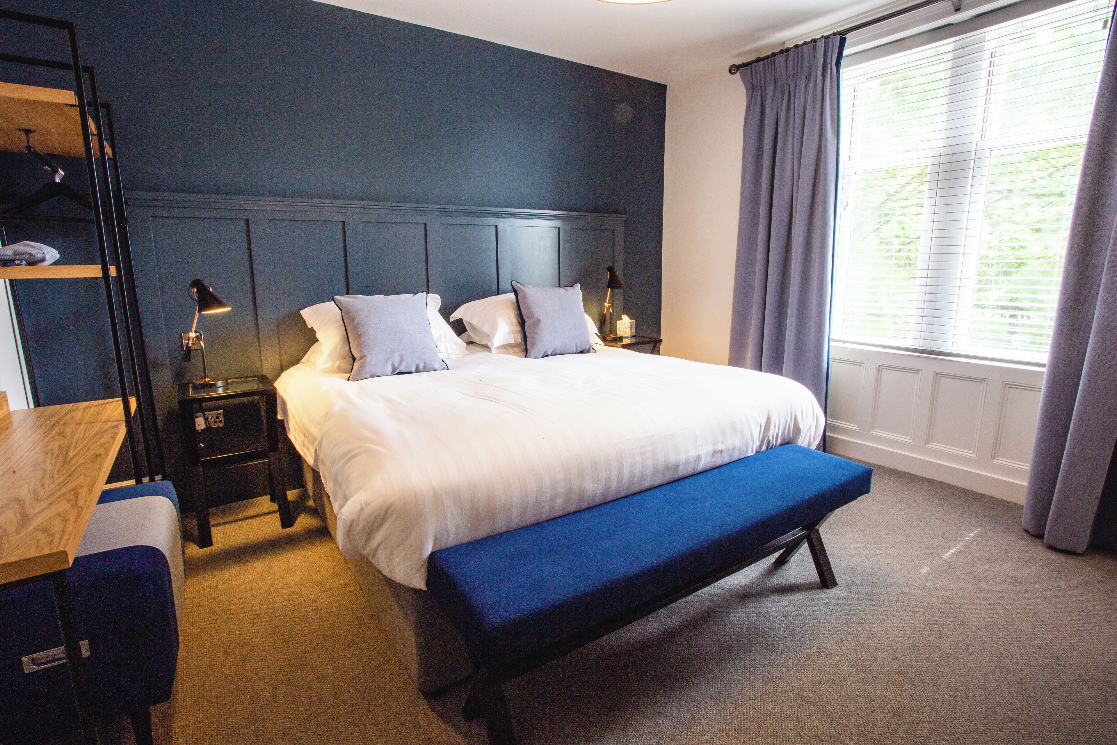 A neatly arranged bedroom with a bed, bedside tables, a bench, and a window with curtains.