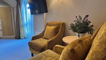 Ett mysigt rum med två fåtöljer, ett litet bord, en väggmonterad TV och en krukväxt.