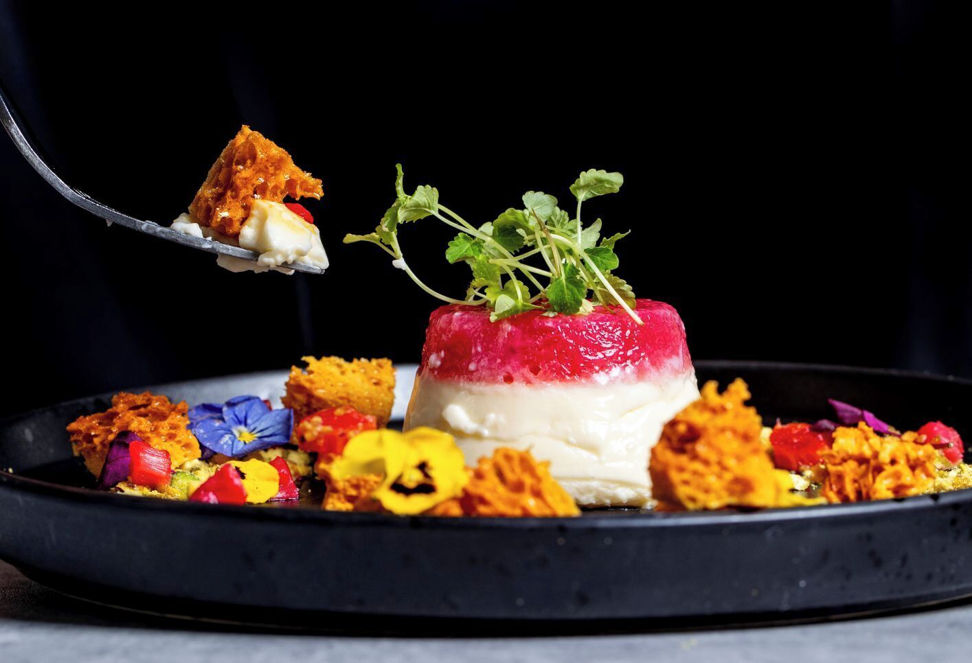 Un dessert à plusieurs couches, décoré de verdure et entouré d’aliments aux couleurs vives.
