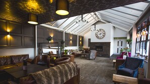 En rummelig lounge med læderpolstrede møbler, pejs og et højt loft med ovenlys.