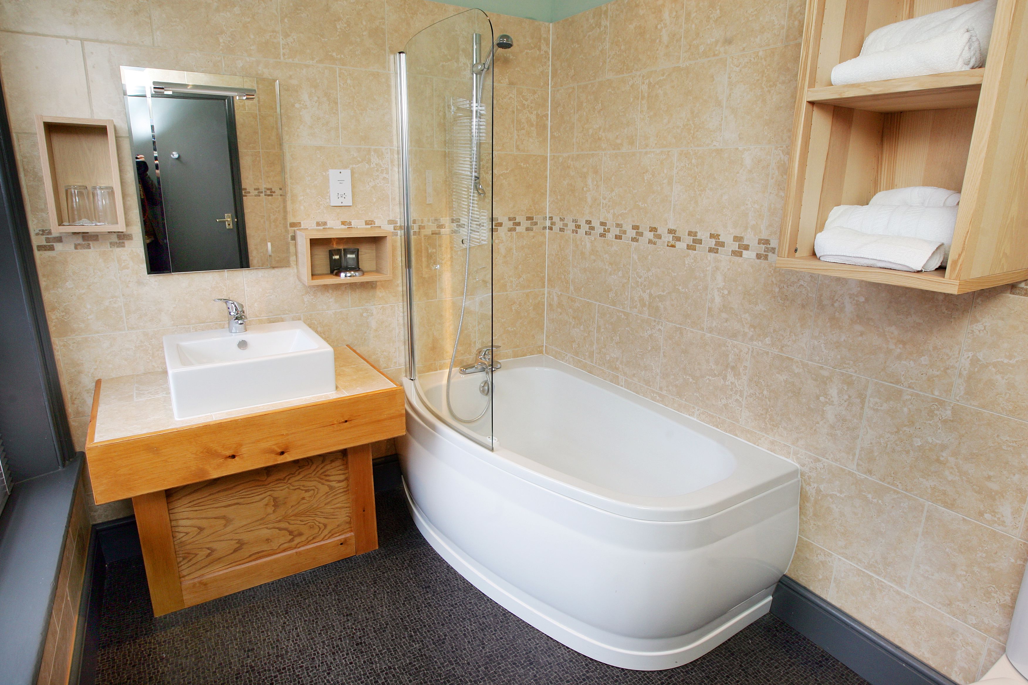 A bathroom with a bathtub, a sink, a glass-enclosed shower, and wooden shelves with towels.