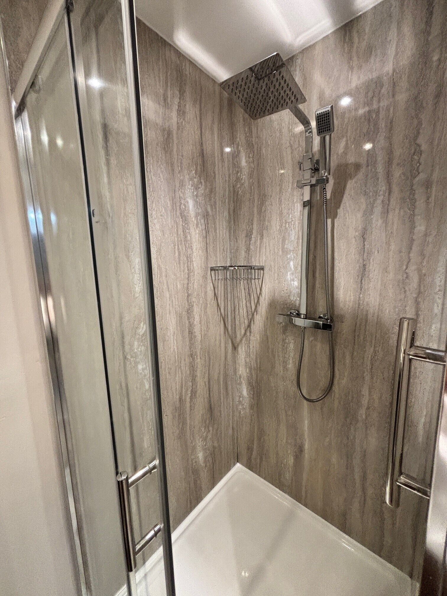 A modern shower with a glass door, a handheld showerhead, and a wall-mounted control panel.