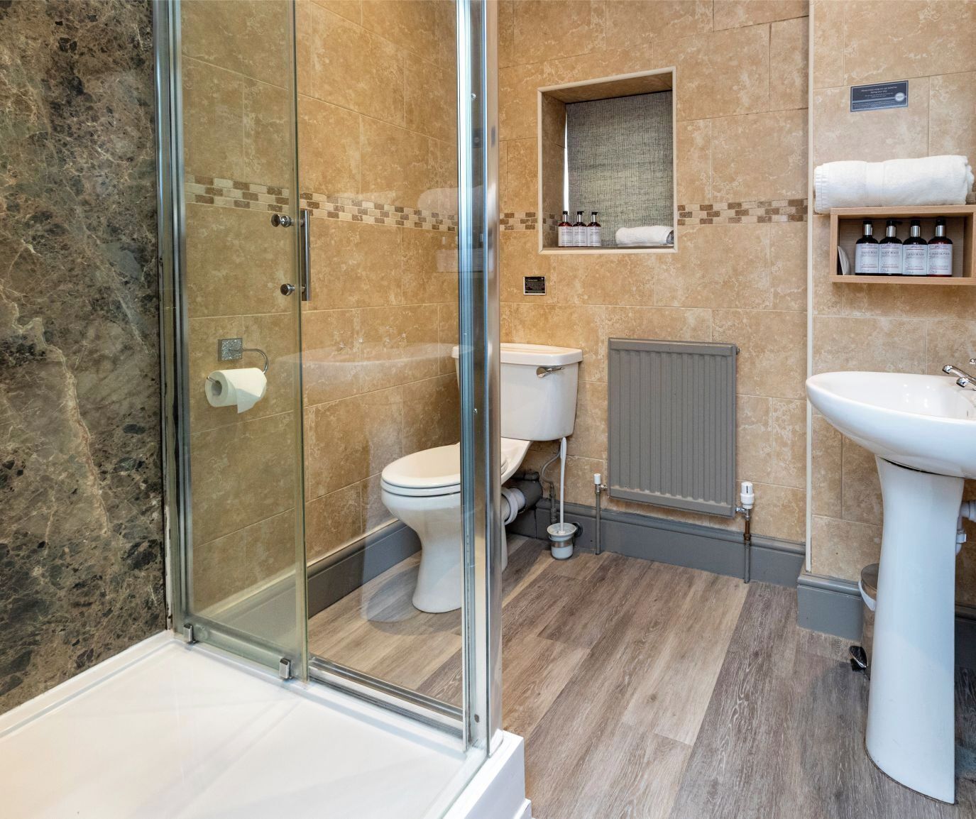 Un baño moderno con cabina de ducha de vidrio, inodoro, lavamanos y toallero con artículos de aseo.