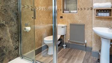 Un baño moderno con cabina de ducha de vidrio, inodoro, lavamanos y toallero con artículos de aseo.