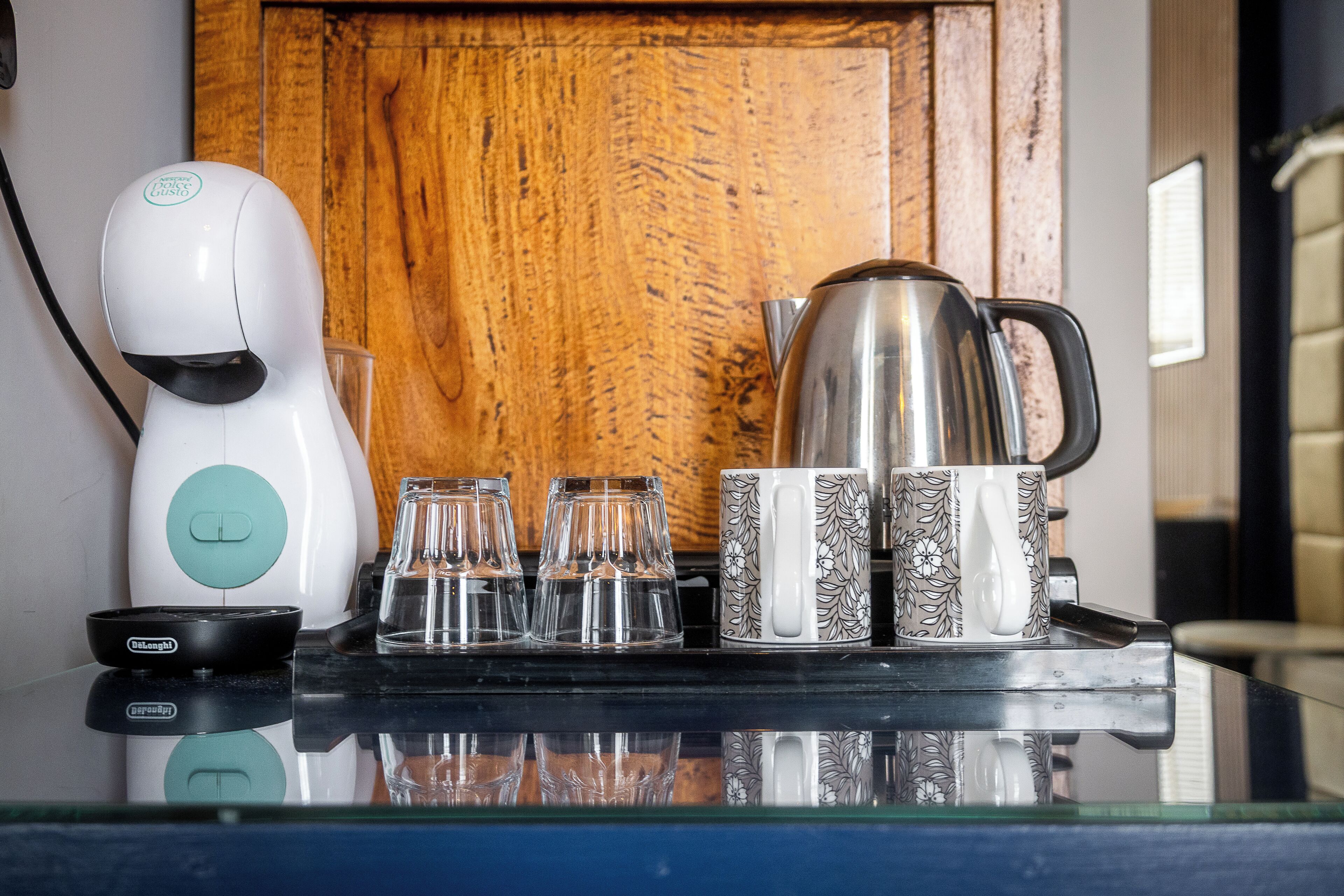 Un comptoir de cuisine avec une machine à café, une bouilloire et un plateau contenant des tasses et des verres.