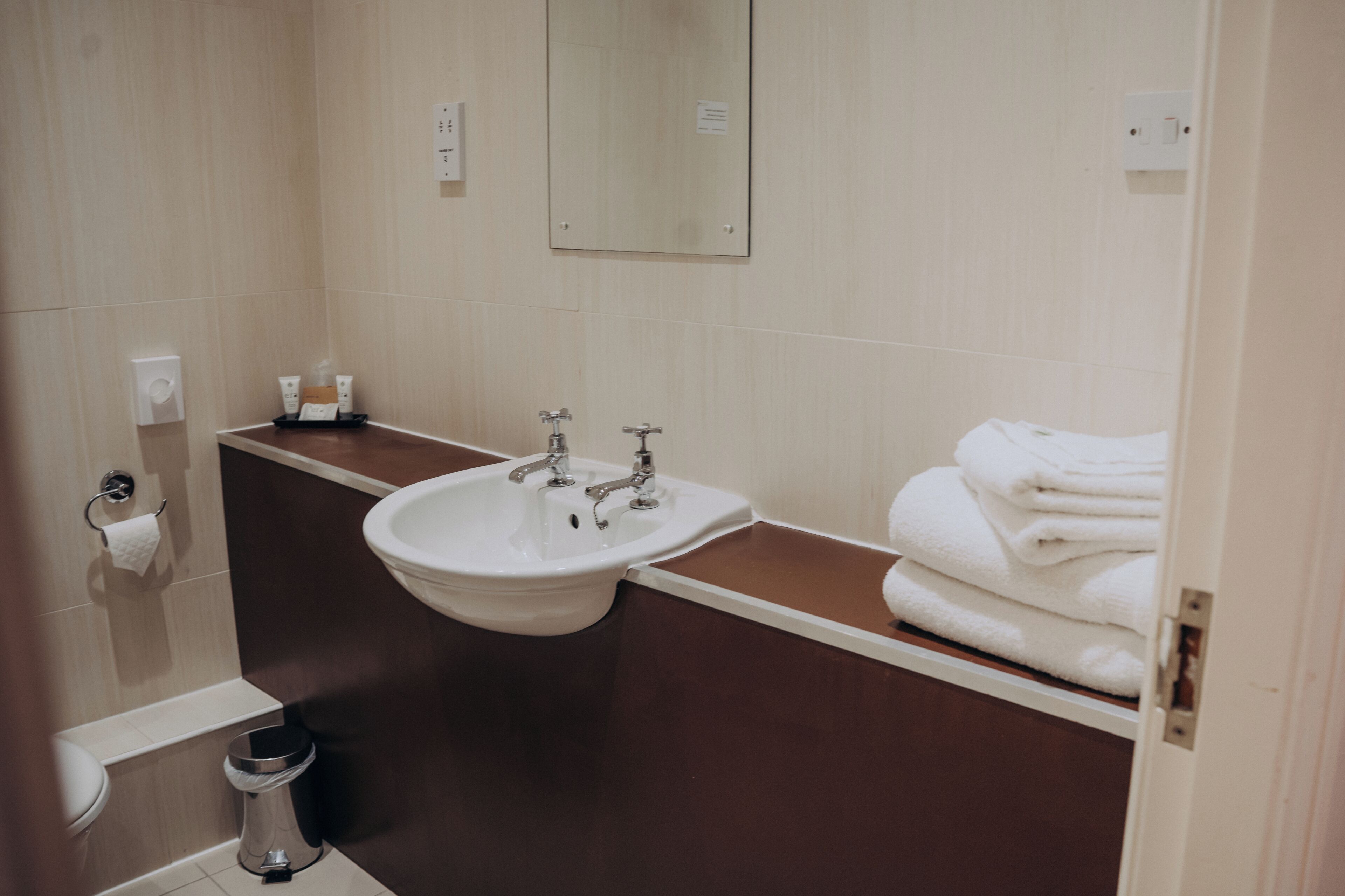 Un baño con lavamanos, espejo, toallero y retrete.