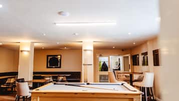 A pool table in a room with a billiards setup, a billiard table, and a seating area with chairs and tables.