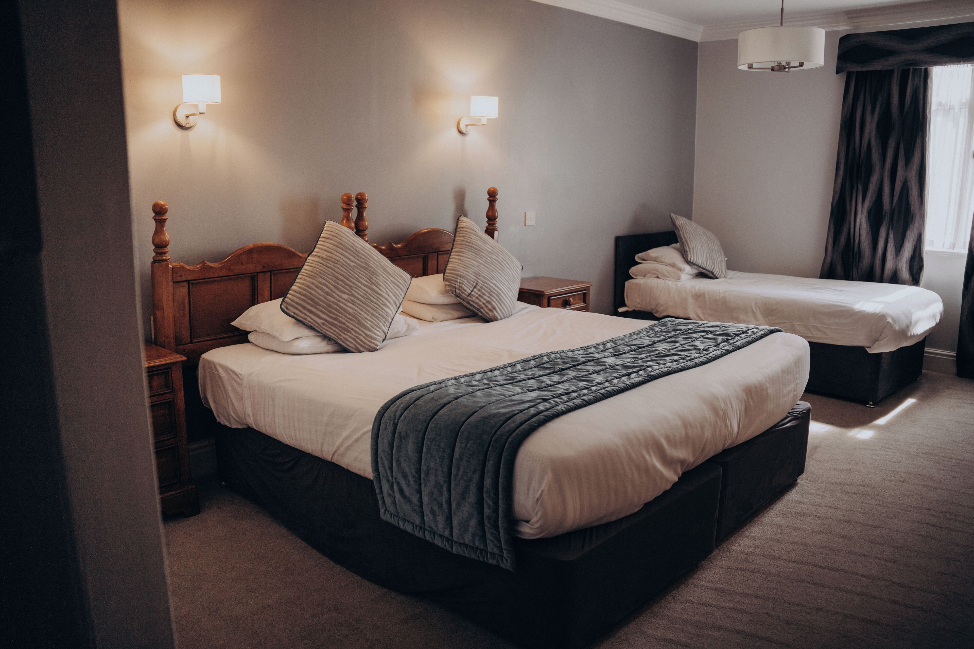 A hotel room with a large bed, a smaller bed, two bedside tables, and a nightstand.