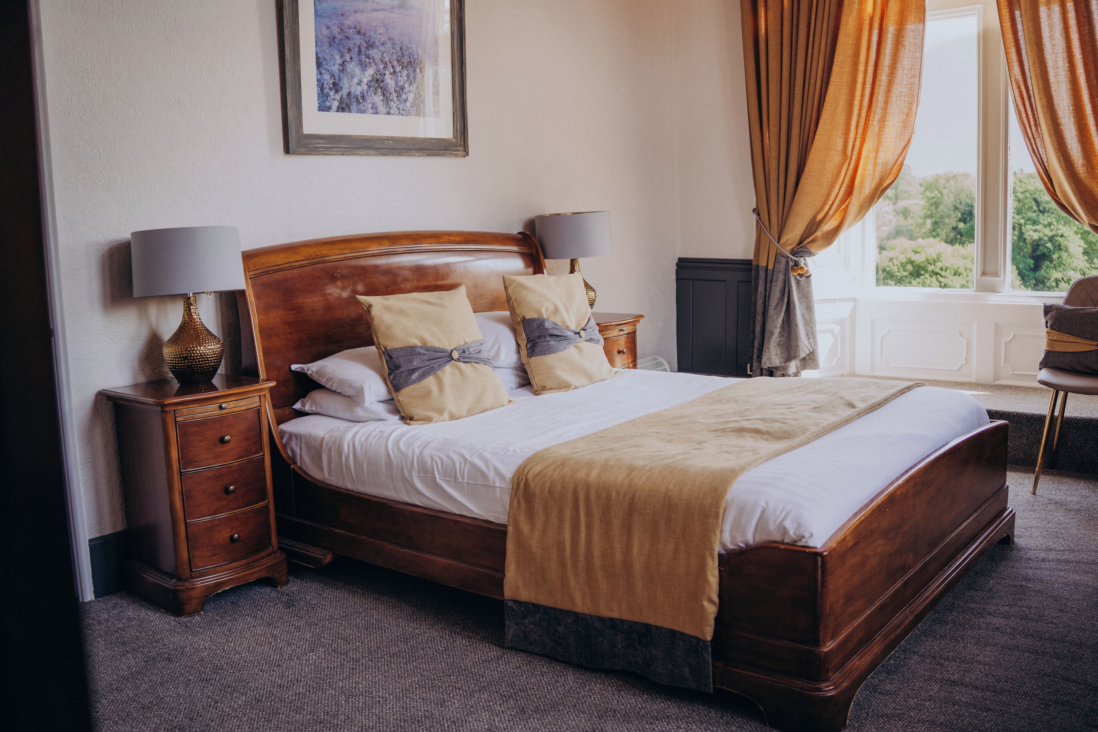 A neatly made bed with a wooden headboard, two bedside tables with lamps, and a window with curtains.
