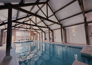 An indoor swimming pool with a high ceiling and wooden beams, surrounded by walls with a mix of brick and plaster. - Cave Castle Hotel  (Brough)
