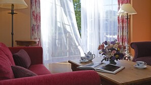 Una habitación acogedora con un sofá rojo, una mesa de madera con un libro, un hervidor y un jarrón con flores.