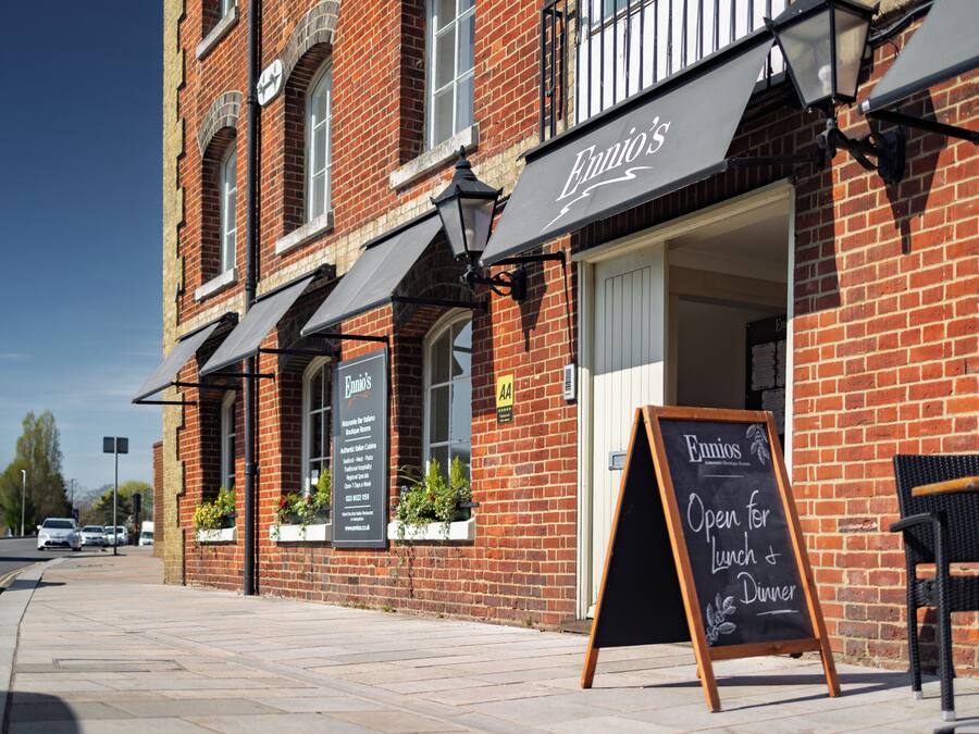 A brick building with a sign reading "Ennios" and a chalkboard sign stating "Open for Lunch & Dinner."