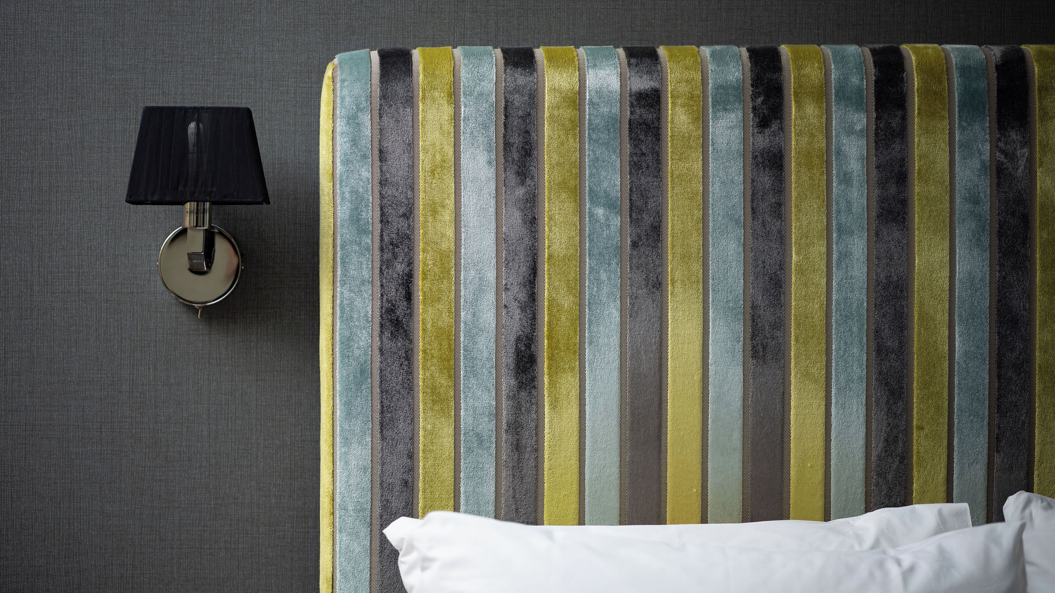 A striped headboard with a round wall-mounted lamp beside it.