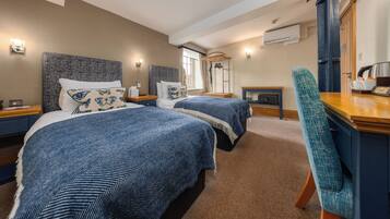 A hotel room with two beds, a desk, a chair, a mirror, and an air conditioning unit.