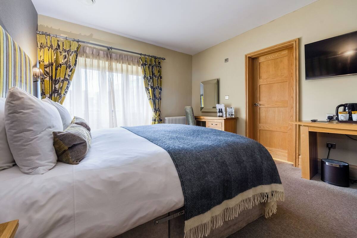 Una habitación de hotel con una cama, un escritorio con computadora, televisor y puerta.