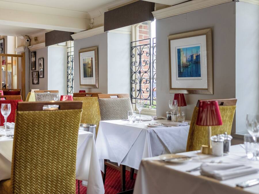 A restaurant interior with tables set for dining, chairs with woven backs, and artwork on the walls.