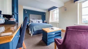 Ein Hotelzimmer mit Bett, Schreibtisch, Computer, Stuhl und Fenster mit Blick auf Gebäude.