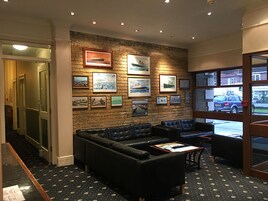 A lobby with a brick wall, framed pictures, a black leather sofa, and a patterned carpet.