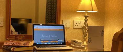 A laptop on a wooden desk with a lamp, a telephone, and books.