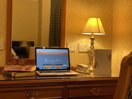 Una computadora portátil sobre un escritorio de madera con una lámpara, un teléfono y libros.