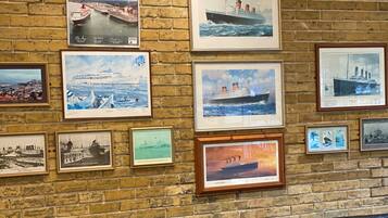 A room with a brick wall adorned with framed maritime paintings, a black leather sofa, and a small round table.