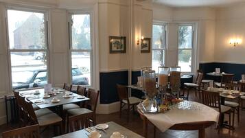 A dining area with tables set for service, large windows with views of the outside, and a wall-mounted light fixture.