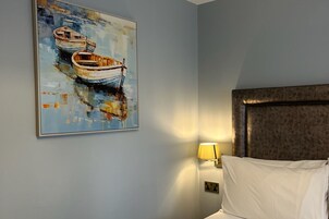 A hotel room with a bed, a painting of boats, a lamp, and a headboard.