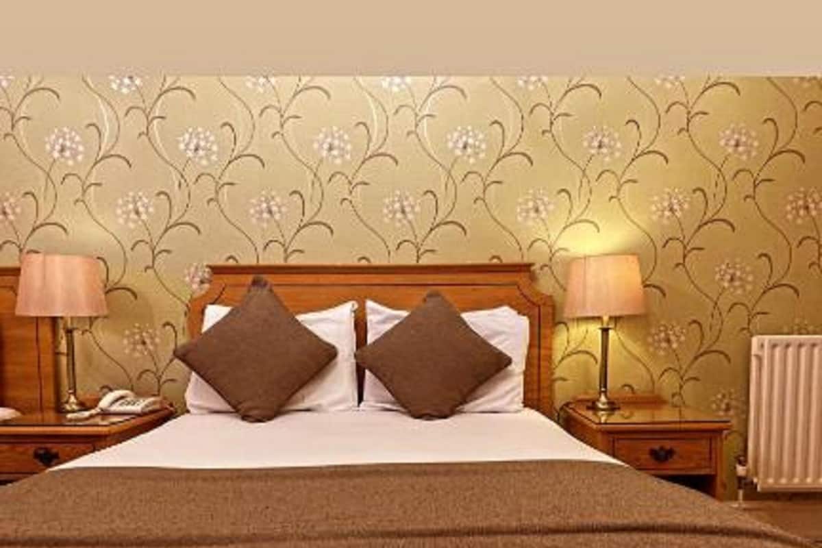 A neatly made bed with two pillows, a bedside lamp, and a nightstand with a phone.