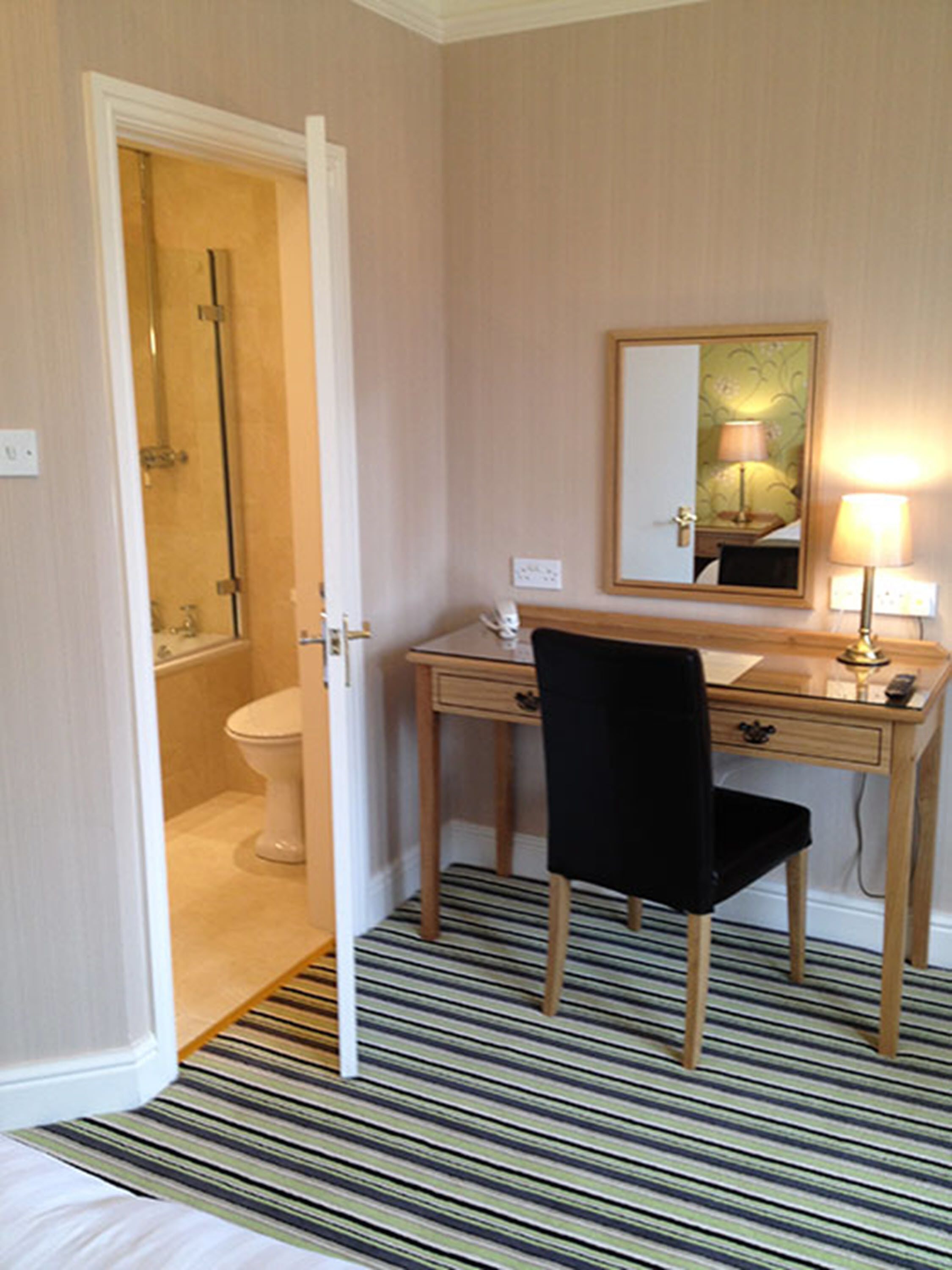 Une chambre d’hôtel avec une salle de bain, un bureau avec une chaise, un miroir et une lampe.
