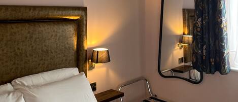 A hotel room with a bed, a nightstand, a lamp, a mirror, and a window with curtains.