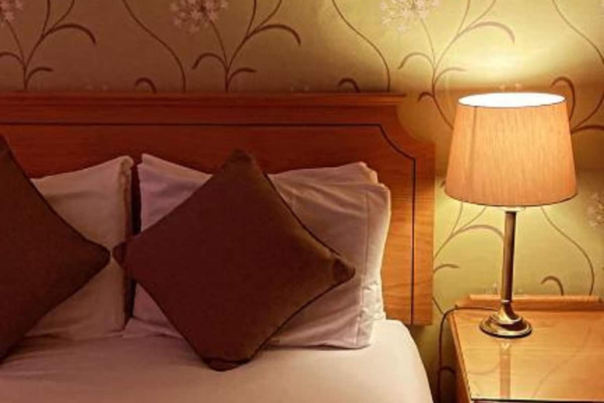 A hotel room with a bed, pillows, a nightstand, and a lamp.