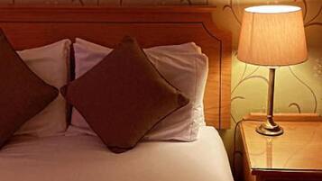 A hotel room with a bed, pillows, a nightstand, and a lamp.