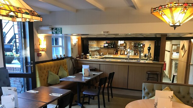 Een restaurant met een bar, zitplaatsen met tafels en stoelen, en uitzicht op het exterieur.