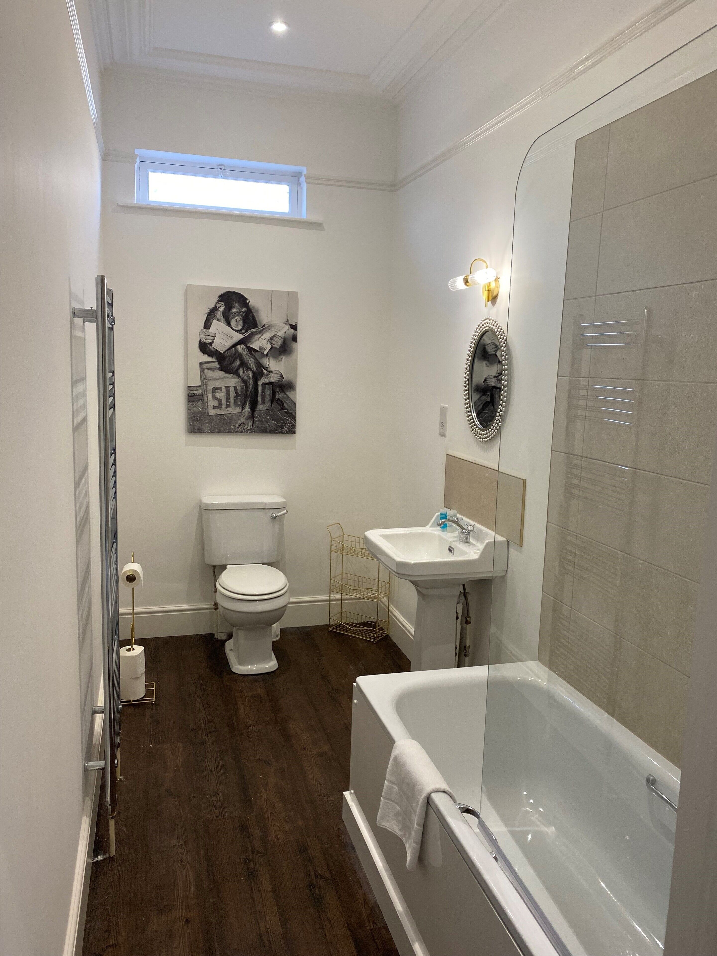 A bathroom with a toilet, sink, and bathtub. There is a painting on the wall and a window above the toilet.