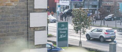A view of The Elizabeth House Hotel sign, a brick building with multiple shops, and parked cars on the street.