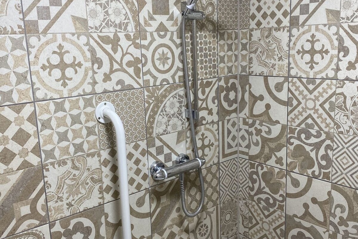 A bathroom with patterned tiles, a shower, a grab bar, and a toilet.