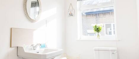 A bathroom with a pedestal sink, toilet, and a window with a view of buildings.