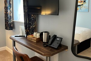 Una habitación de hotel con un escritorio de madera, un teléfono, un hervidor de agua y una cama con ropa blanca.