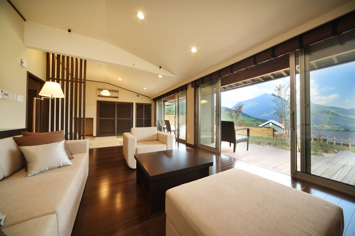 A modern living room with a sofa, armchair, and a coffee table. There is a large window offering a view of the outdoors.