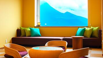 A room with a sofa, chairs, a small table, and a large window with a mountain view.