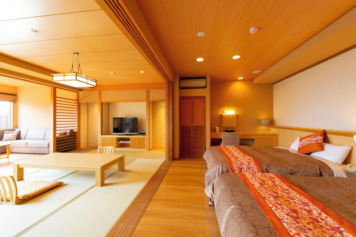 A hotel room with a wooden floor, a sofa, a TV, a desk, and two beds with patterned bedding.