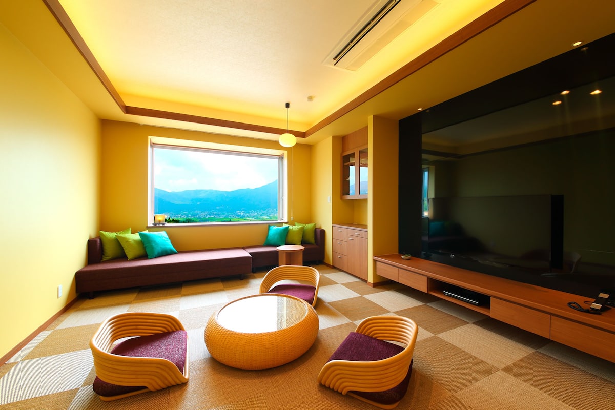 A modern living room with a large TV, comfortable seating, and a view of the outdoors.