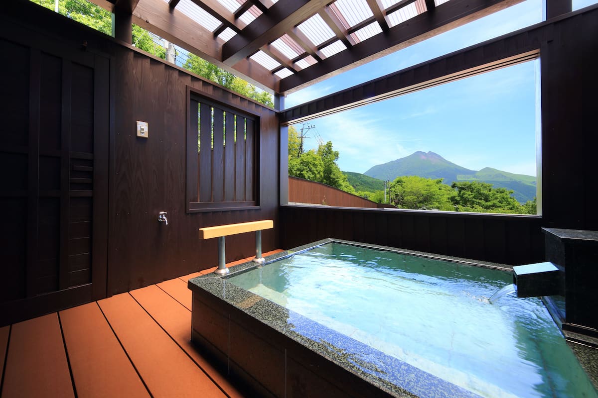 A hot tub with a view of a mountain, wooden deck, and a window with a view of greenery.