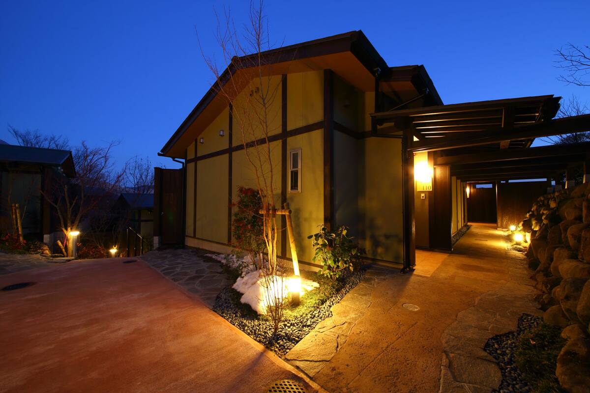 A modern house with a stone pathway leading to the entrance, a covered porch, and a well-lit driveway.