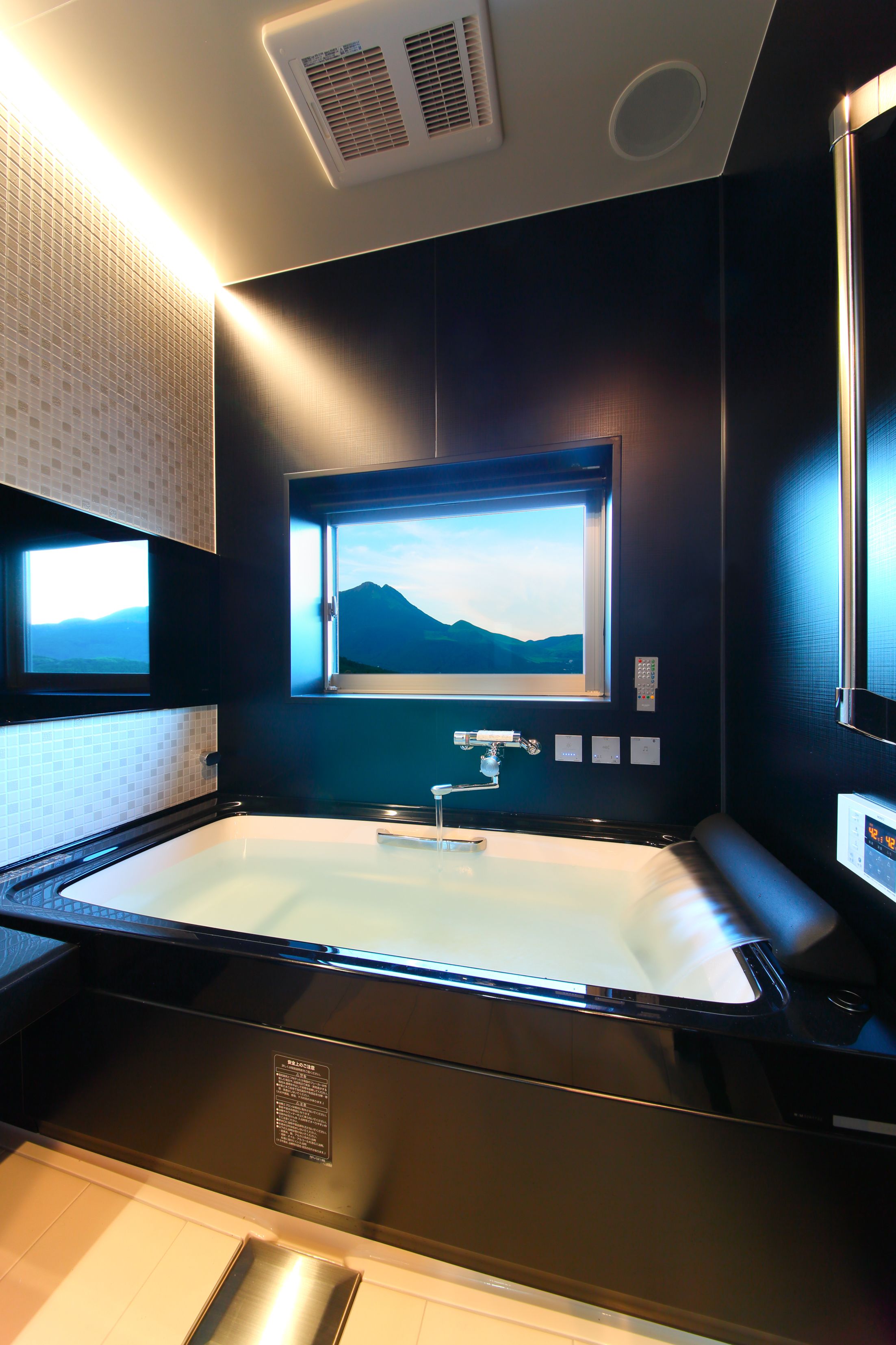 A modern bathroom with a large bathtub, a window with a mountain view, and a control panel on the wall.